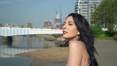 slow motion of a beautiful latina woman on holiday leaning against the railing, looking at the river thames in london and waving with her hand, smiling and wandering