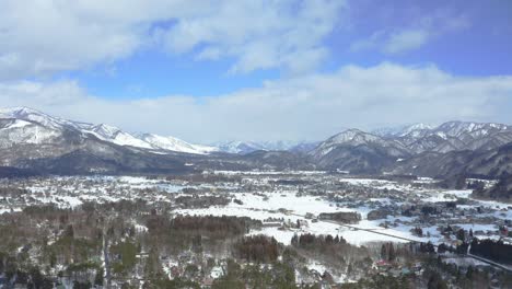 Through-aerial-cinematography,-a-vivid-portrait-of-Hakuba-valley-and-it's-city-in-Japan-during-winter,-showcasing-the-breathtaking-combination-of-snow-capped-scenery,-lush-forests,-and-urban-life