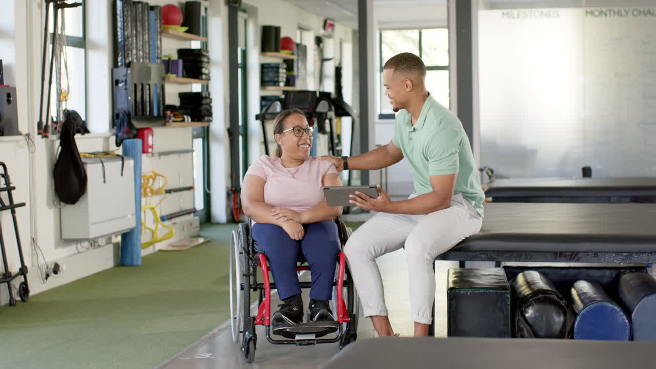 Rehabilitation center, therapist using tablet and supporting woman with paraplegia in wheelchair