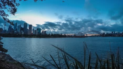 Timelapse-Con-Gran-Angular-Del-Horizonte-De-Sydney-Y-La-ópera-Y-El-Puente-Del-Puerto-Al-Atardecer-En-Un-Día-Nublado-Con-Hermosos-Colores-Tomados-De-La-Silla-De-La-Señora-Macquarie