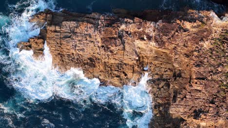 Atemberaubender-Blick-Von-Oben-Auf-Eine-Schroffe-Klippe,-Die-Auf-Das-Turbulente-Azurblaue-Wasser-Trifft:-Der-Kontrast-Der-Natur-Im-Spiel