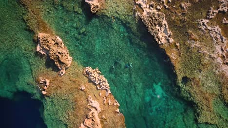 Drone-shot-flying-downwards-towards-divers-in-crystal-clear-seas-in-Cirkewwa-Malta