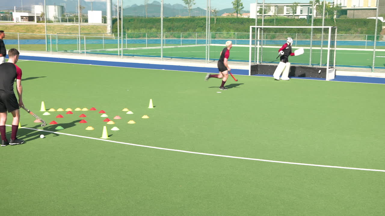 Practicing field hockey, men running drills with cones on outdoor turf field