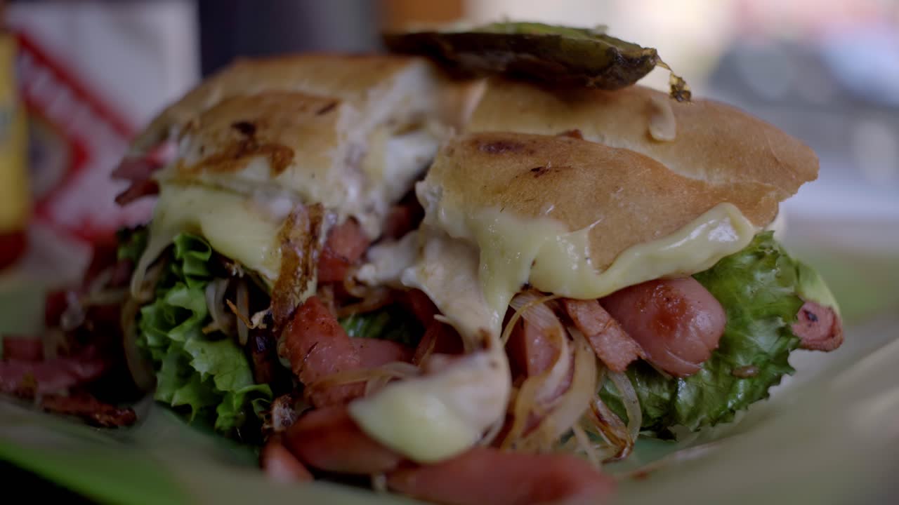 Ripresa semi-orbitale di un panino grigliato da strada ripieno di carne, lattuga e formaggio fuso su un piatto.