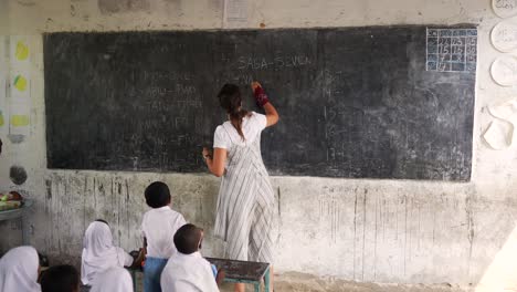 white caucasian teacher writing on the blackboard numbers teaching black african children