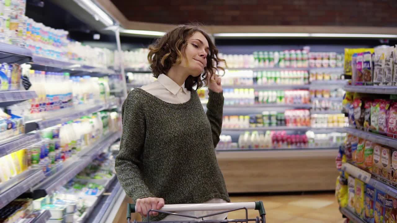 슈퍼마켓에서 행복한 젊은 여성은 선반에 있는 상품과 유제품을 통해 춤을 추고 있습니다. 회전하고, 재미있고, 긍정적입니다.