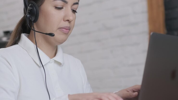 Operátorka call centra a agentka zákaznické podpory se sluchátky konzultuje klienta online, píše na notebooku, hovoří v internetovém chatu a uskutečňuje konferenční videohovor.