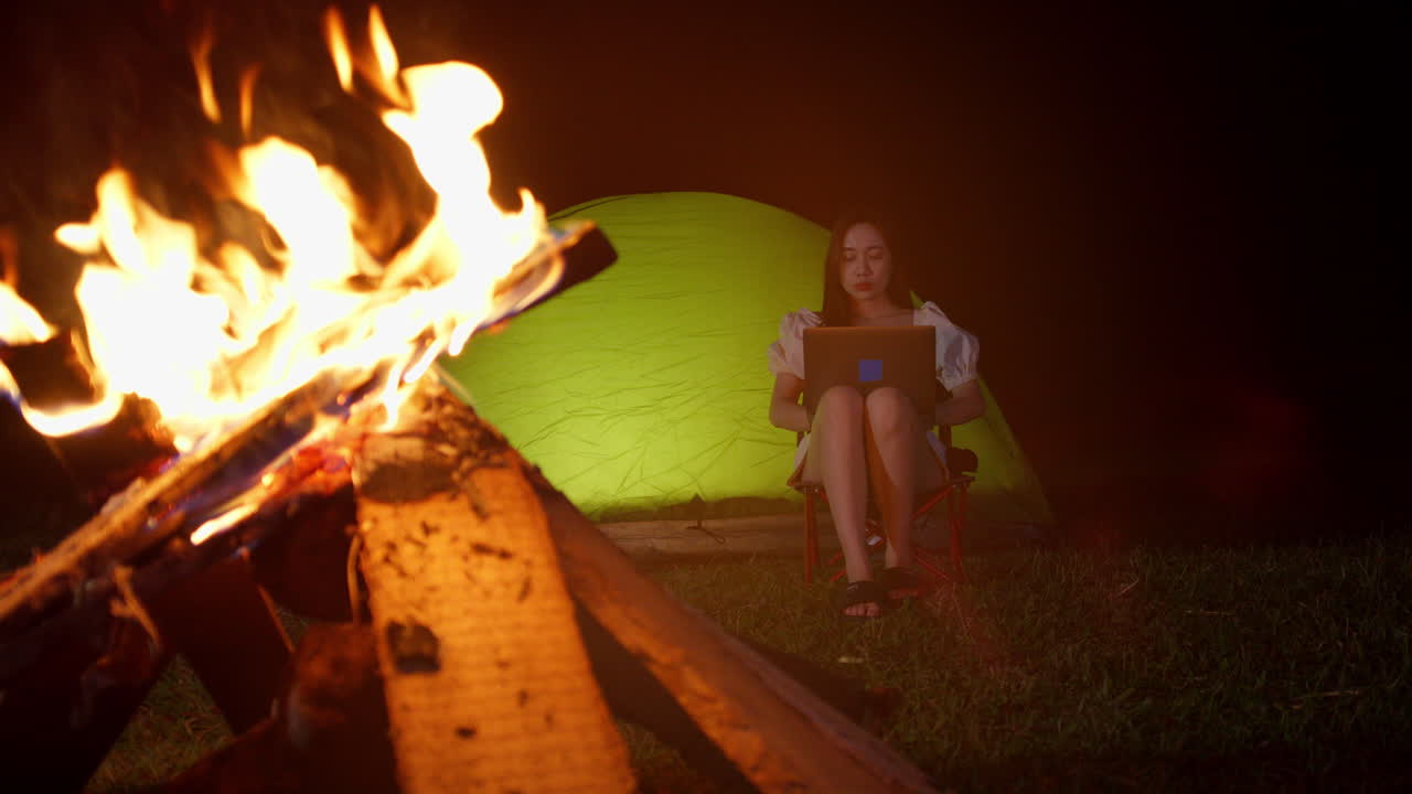 nómada digital trabajando remotamente desde un destino remoto frente a una fogata mientras acampa al aire libre
