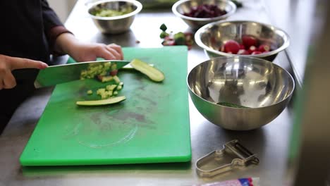 un trabajador de la cocina cortando un pepino en una tabla de corte verde dentro