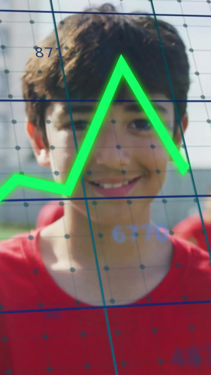 Vídeo vertical: Menino de uniforme vermelho sorrindo enquanto dados são atualizados, criando gráficos de linha sobre o rosto para esportes.