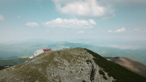 drone shot of top of the snežnik mountain with a half hidden mountain cottage with red roof