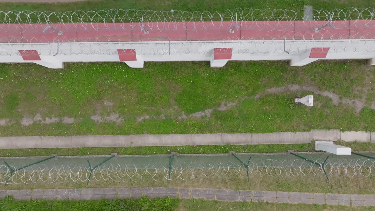 Drone reveal shot showing detailed barbed wire fence and high prison wall illuminated by sunlight