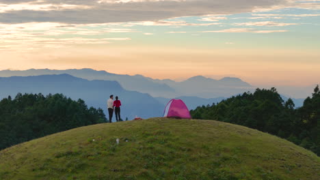 una hermosa toma de dron captura a una pareja de pie fuera de su tienda en sailung, dolakha, nepal, presenciando el amanecer disfrutando de los vibrantes colores de la naturaleza, la exuberante vegetación y las colinas en una mañana pacífica