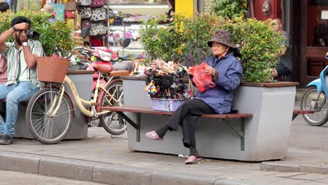 vendor arranging flowers, cyclist on phone nearby