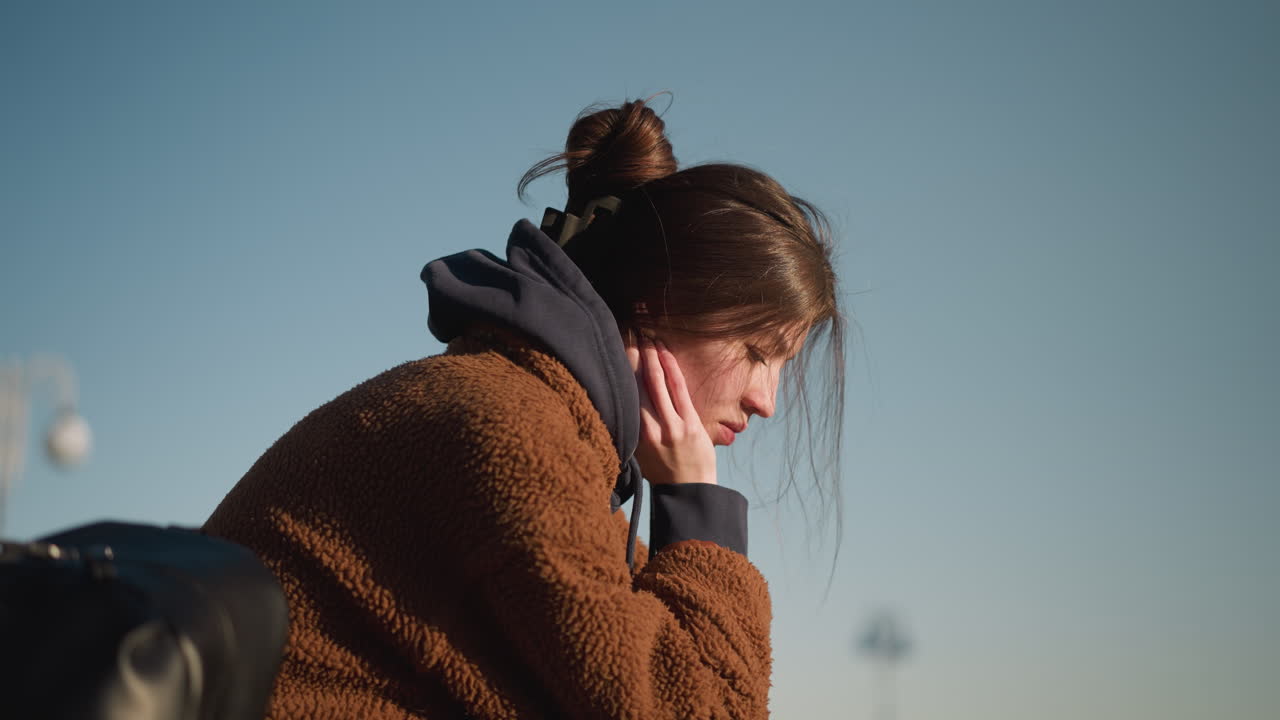 갈색 코트를 입은 소녀의 클로즈업, 깊은 혼란과 생각에 빠진 모습, 그녀의 감정 상태를 강조합니다. 배경은 은 하늘입니다.