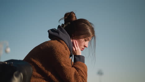 a close-up of a girl wearing a brown coat, looking deeply disturbed and lost in thought. emphasizing her emotional state. the background is a clear sky