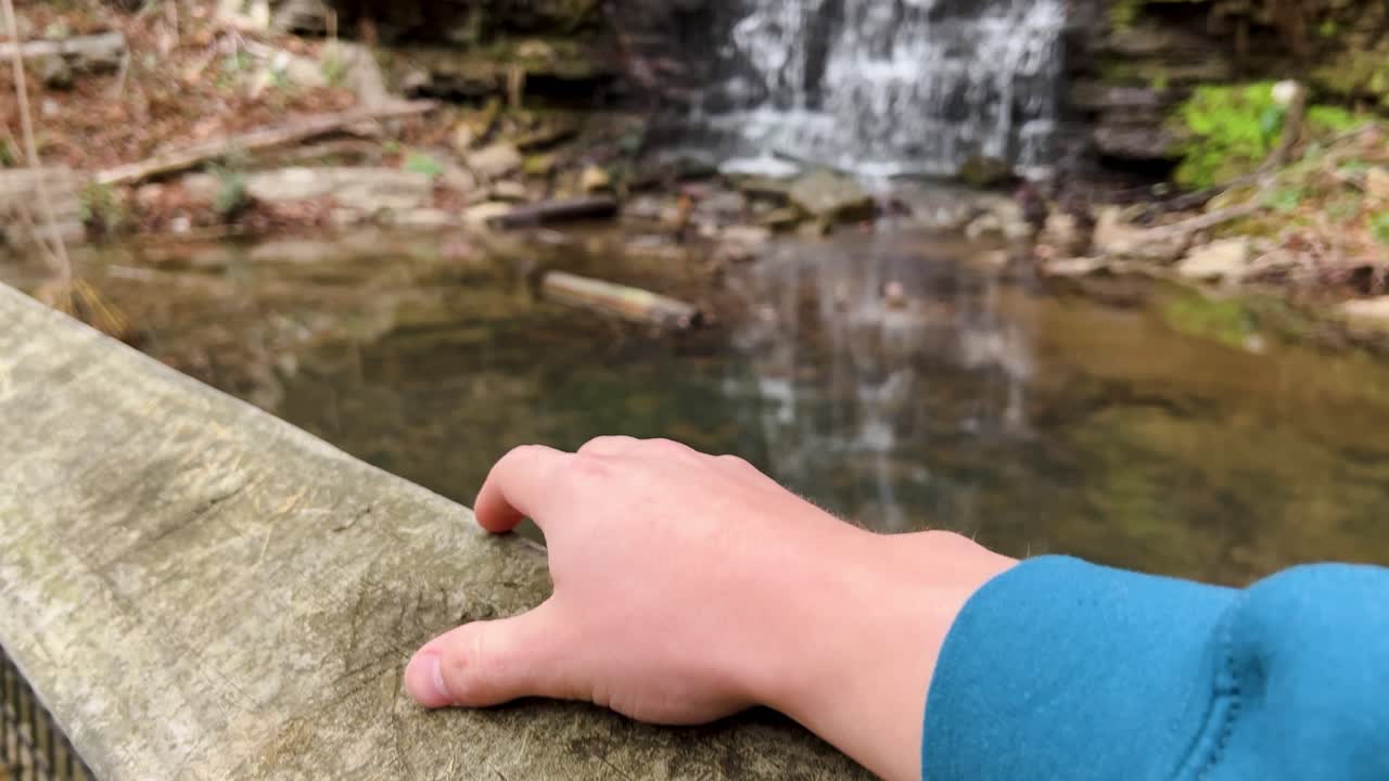 clip de cámara lenta de un hombre tocando su dedo en una barandilla de madera viendo una hermosa cascada en cove spring park frankfort kentucky usa 4k