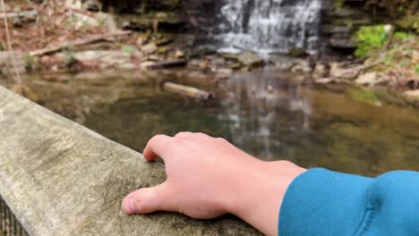 Zeitlupenclip-Eines-Mannes,-Der-Mit-Dem-Finger-Auf-Ein-Holzgeländer-Tippt-Und-Einen-Wunderschönen-Wasserfall-Im-Cove-Spring-Park-Frankfurt,-Kentucky,-USA-4k-Beobachtet