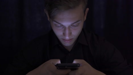 un joven mirando su teléfono, enviando mensajes de texto.