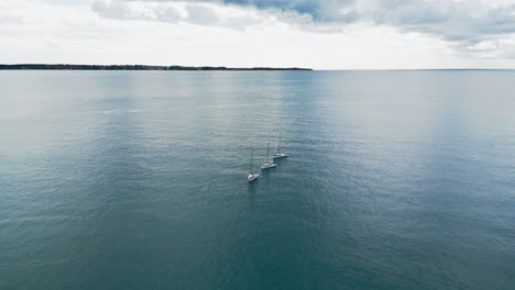 Drohnenaufnahmen-Von-Drei-Segelbooten,-Die-Bei-Bewölktem-Wetter-Mit-Heruntergelassenen-Segeln-Mitten-Im-Meer-Vor-Anker-Liegen