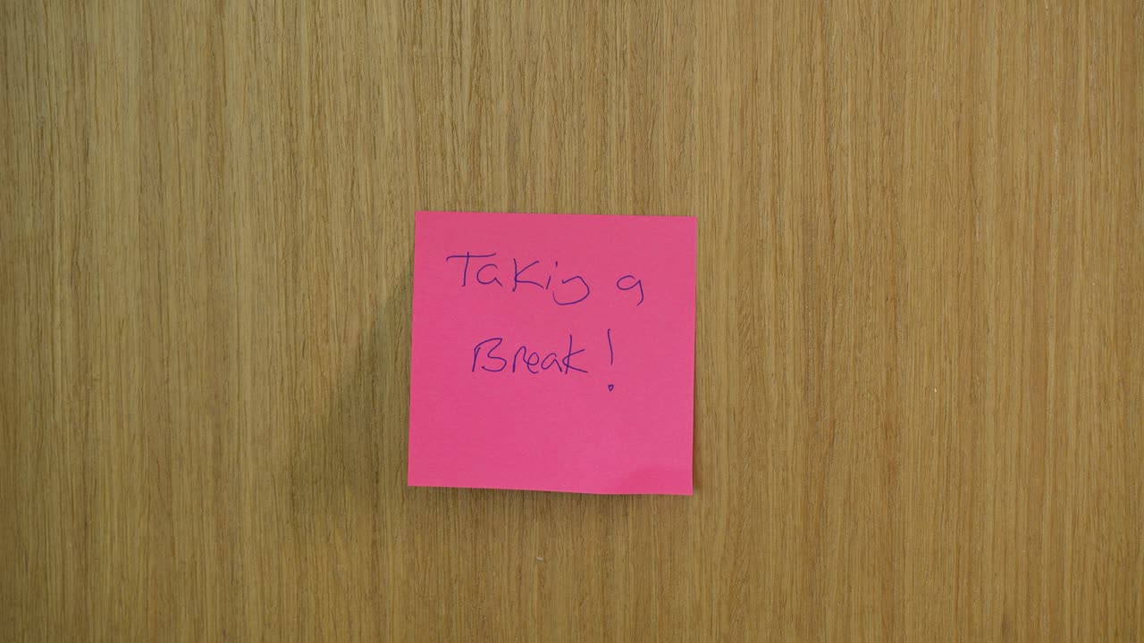 Hand seen placing a post it note on a door that says "taking a break!" - pink paper note displays break message
