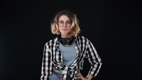 Serious-young-woman-in-black-and-white-plaid-shirt-and-headphones-on-neck,-doing-NO-gesture,-disappointed-gesturing-isolated-on-black-background-in-studio.-People-sincere-emotions