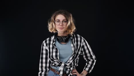 serious young woman in black and white plaid shirt and headphones on neck, doing no gesture, disappointed gesturing isolated on black background in studio. people sincere emotions