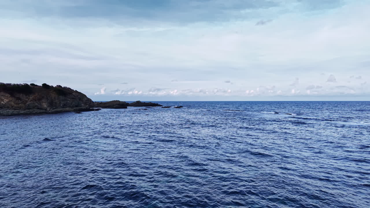 Samudra biru luas membentang di bawah langit yang lembut, di mana ombak tenang bertemu pantai berbatu yang damai saat senja