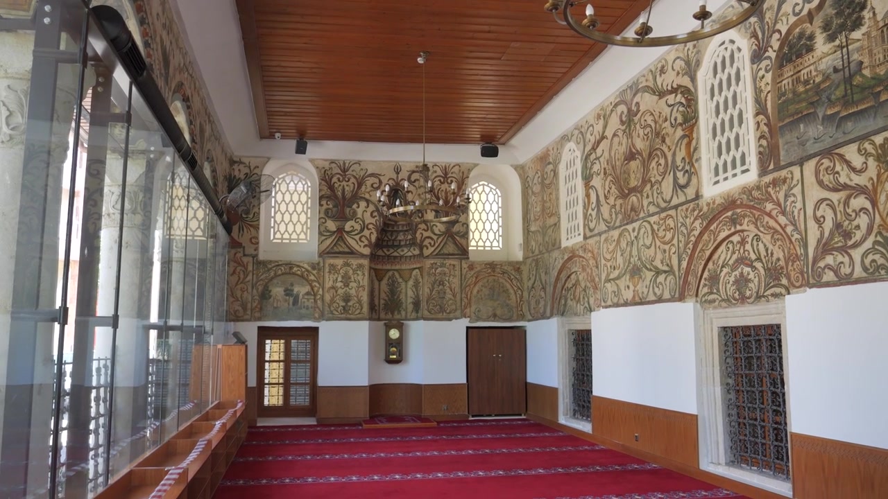 Pareti dipinte ornate, tappeto rosso e lampadari in metallo adornano la sala di preghiera della Moschea di Et'hem Bej. Panoramica