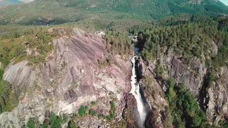 backwards drone shot of a large waterfall in norway and a green forest in the background