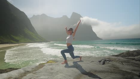 Woman-practicing-yoga-on-Kvalvika-Beach,-Lofoten,-Norway,-during-a-sunny-day,-slow-motion