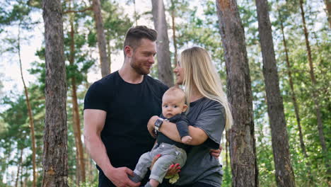 beautiful caucasian couple with their child stand together. happy parents spend good time all together in the forest. low angle view.