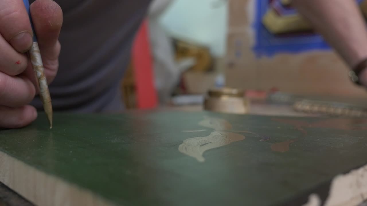 Close-up of an artisan using a brush to paint decorative patterns on a wooden panel. Gilding and painting technique on a Mudéjar coffered ceiling