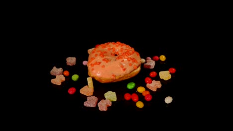 orange funny surprised glazed donut with sprinkles, striped caramel candies, colorful dragee with raisins or peanuts inside rotate on black background