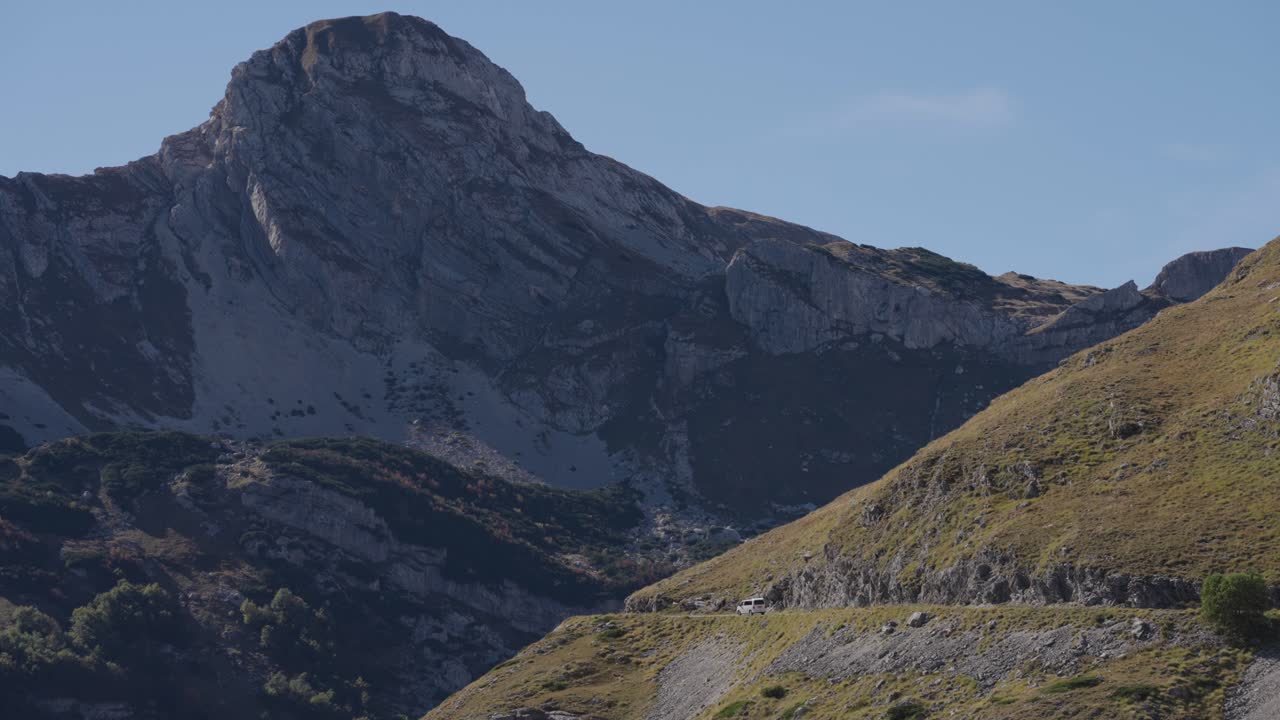 Tele view single white car driving on edge of a steep mountain in Durmitor, Montenegro