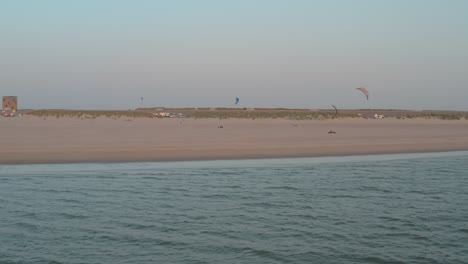 dron cinemático: panorama aéreo que rodea la playa natural verde y arenosa al atardecer con turistas y personas con buggykiting en zelanda en el mar del norte, países bajos, 25p