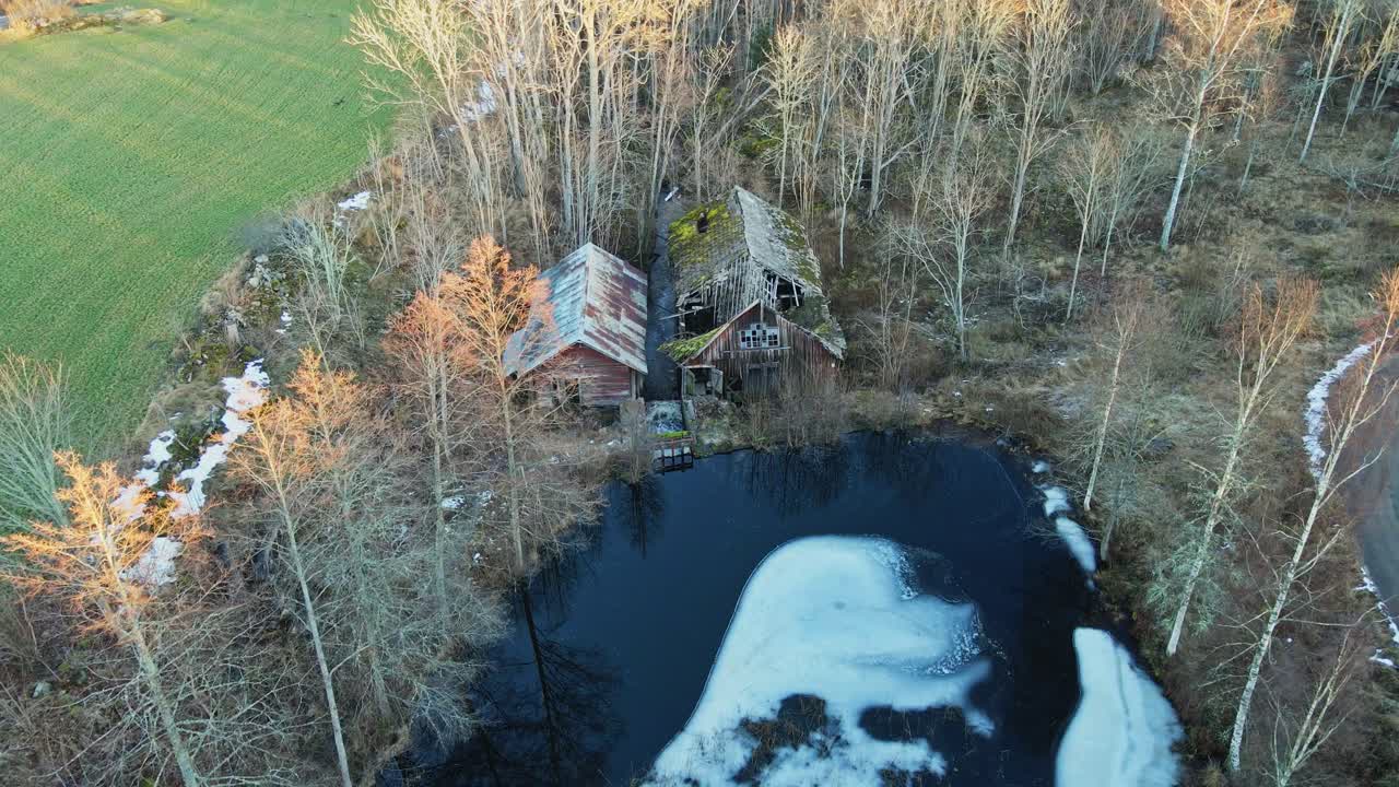 Aerial of an old, abandoned saw mill in rural Sweden. The collapsed structure is near a frozen lake in a forest