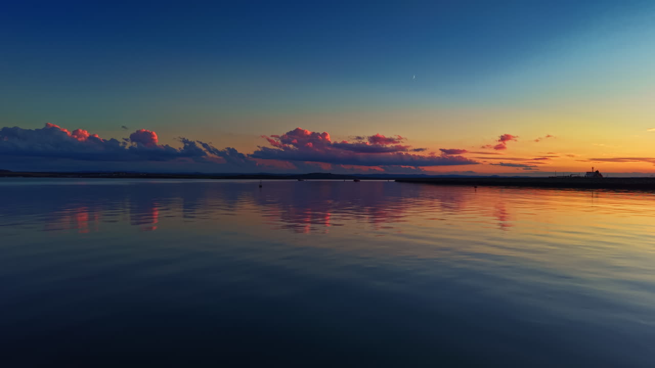 Stunning sunset over calm water with vibrant colors reflecting on the surface at a peaceful shoreline