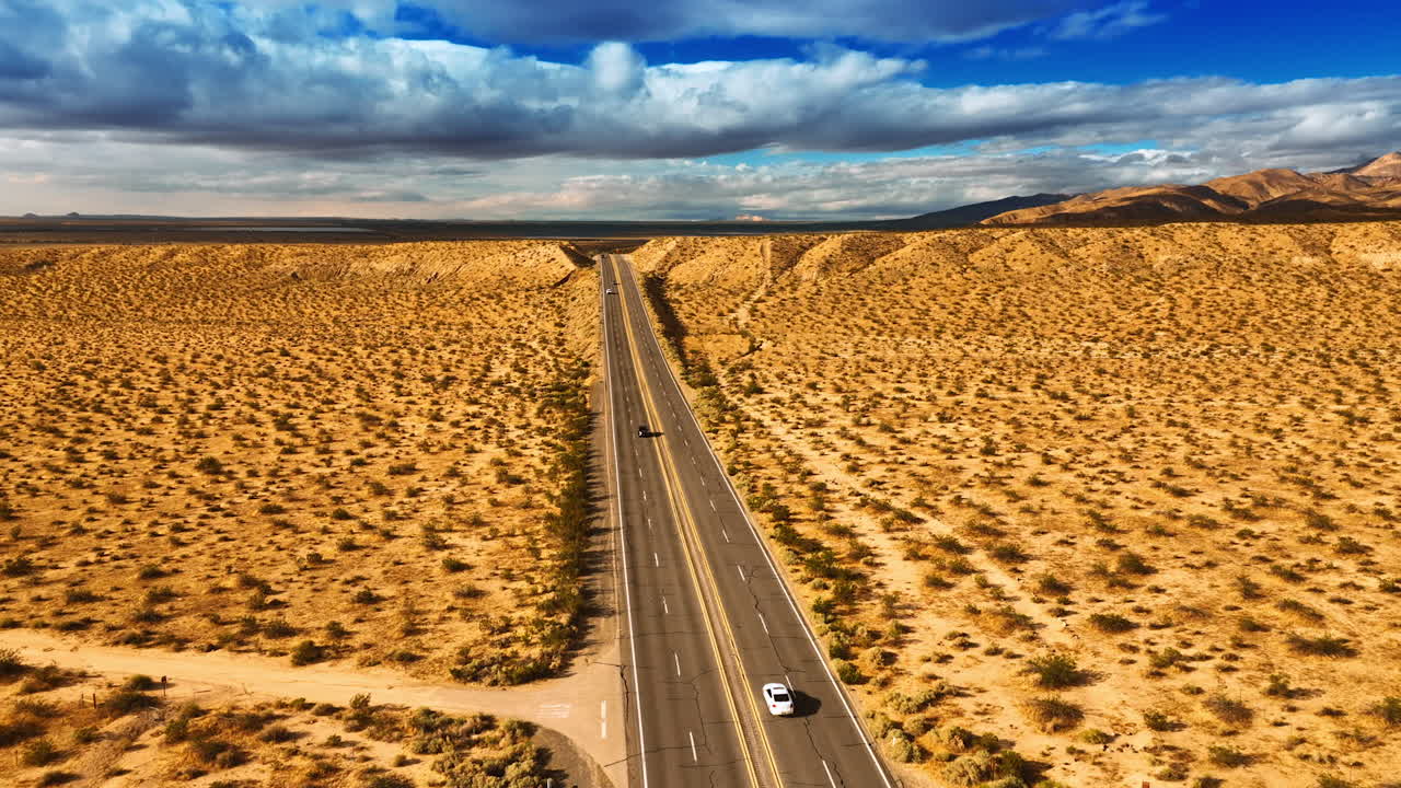 Drone moving above the four-lane highway in the dry desert. Arid landscape in California. Dramatic cloudscape in the sky at backdrop. Top view.