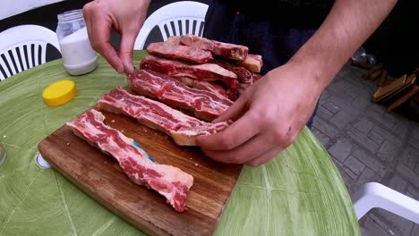 video of a white man putting salt on the raw meat on a wooden board, before grilling