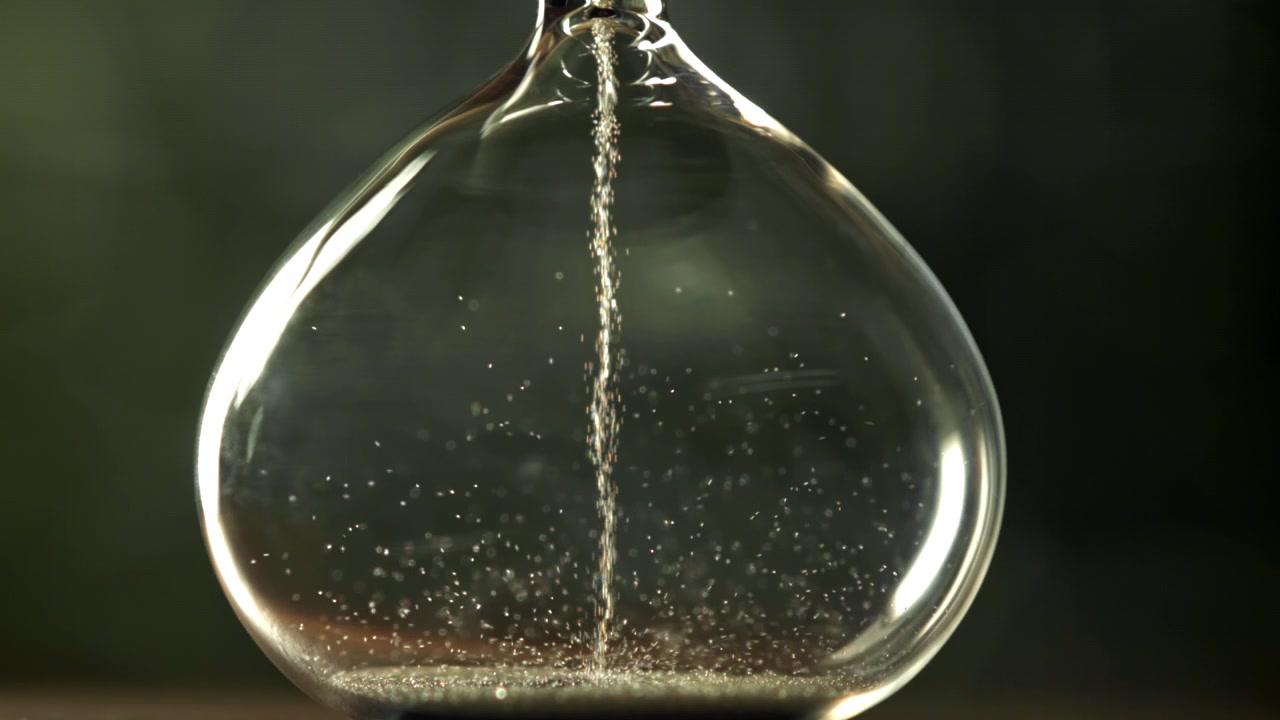 Sabbia che scorre in una clessidra di vetro, a simboleggiare il tempo che passa.