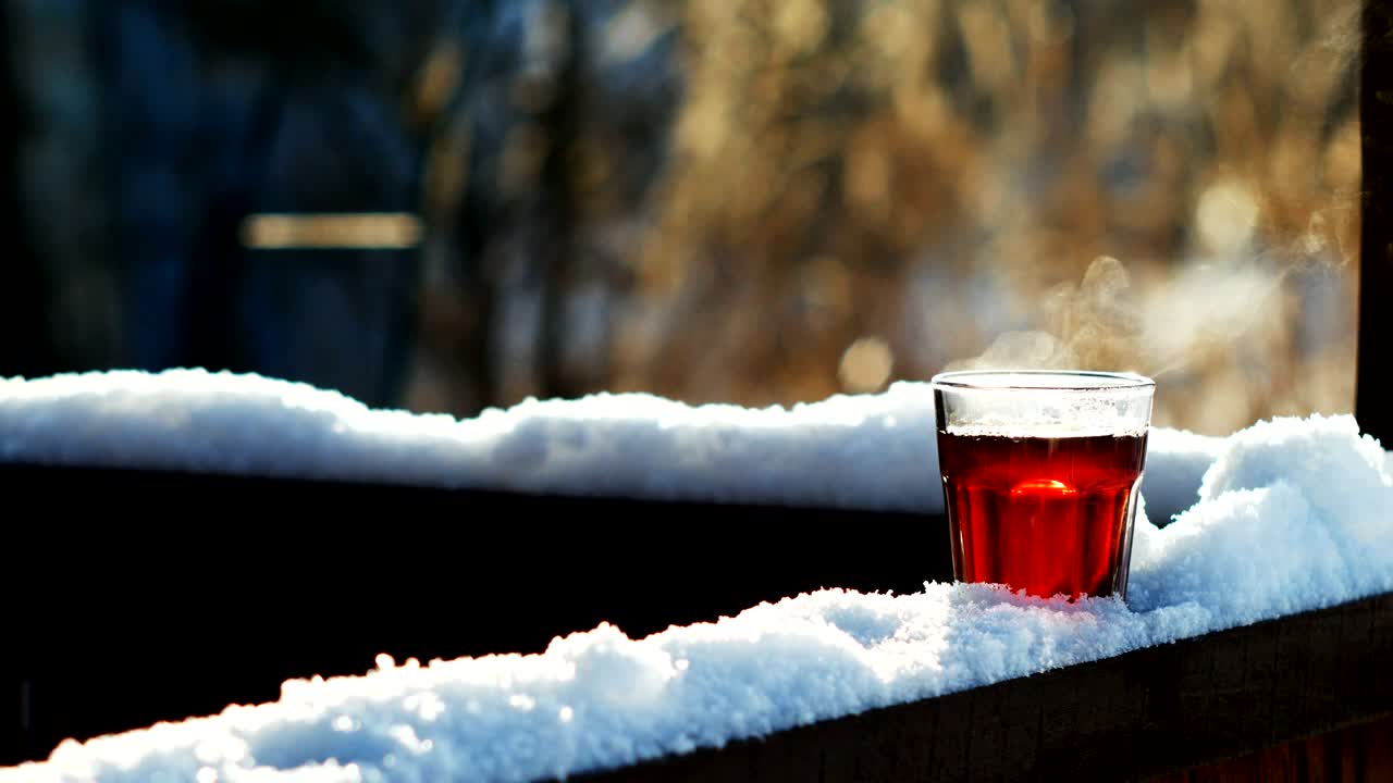 Steaming tea in a glass standing on snow at tree branch, closeup shot