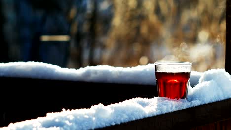 steaming tea in a glass standing on snow at tree branch, closeup shot