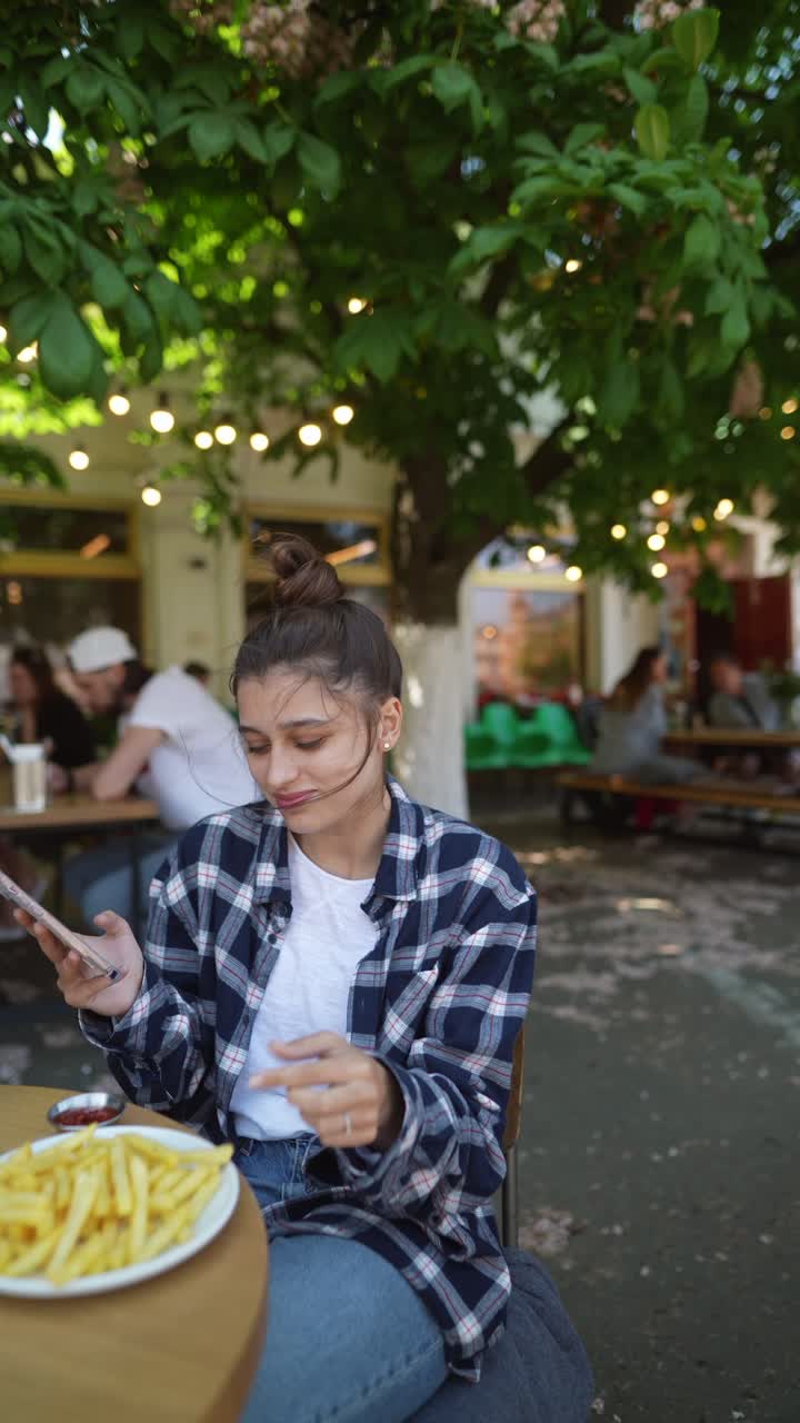 una mujer joven comiendo papas fritas en un café al aire libre