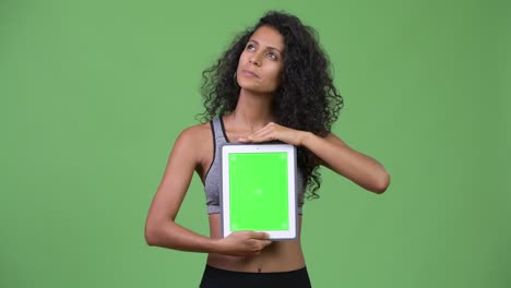 young beautiful hispanic woman with gym clothes showing digital tablet