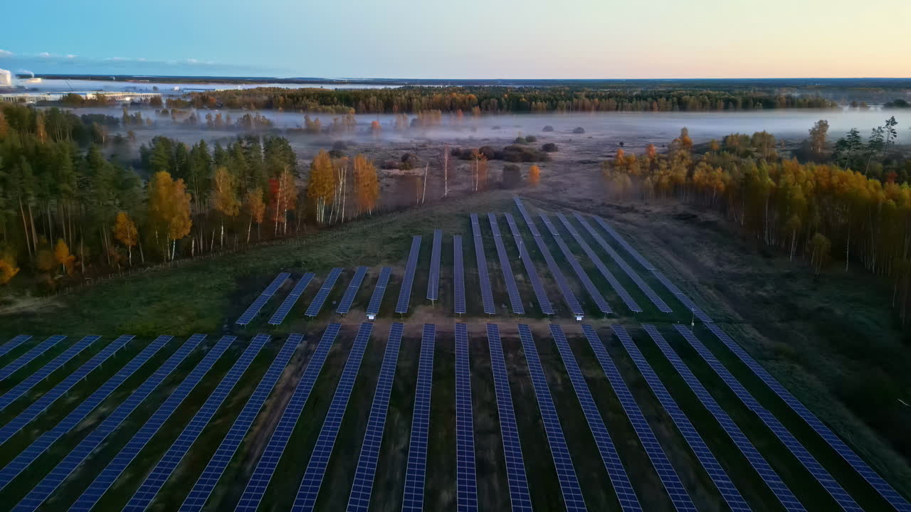 Aerial shot capturing solar farm installed on green field with layers of fog moving around field during morning