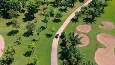 golf cart driven through narrow road path inside huge golf course grounds - aerial view
