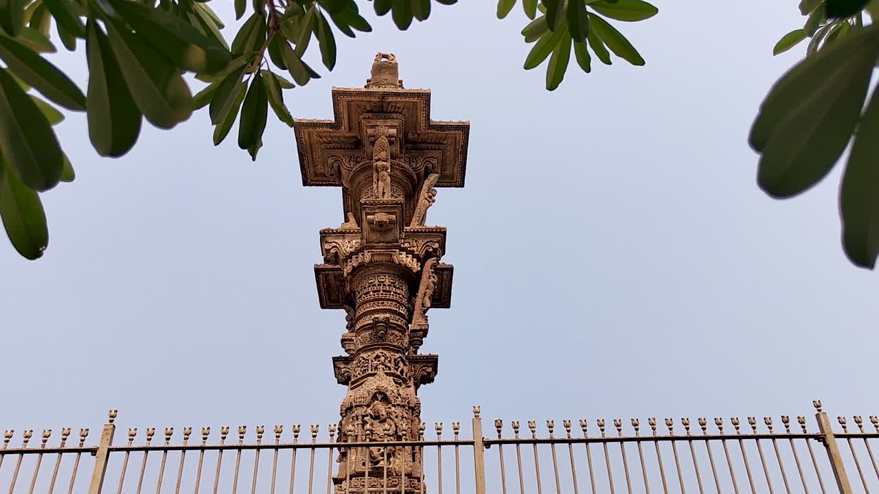 Vadnagar, Gujarat, India: pilastro in pietra Kirti Toran che si erge verso il cielo, incorniciato da foglie di alberi verdi, architettura indiana antica, monumento scolpito, punto di riferimento del patrimonio culturale e sito turistico storico