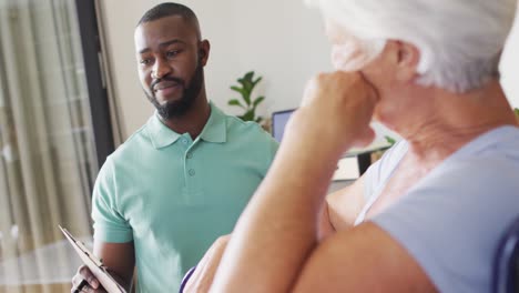 Video-of-happy-african-american-male-physiotherapist-examining-caucasian-senior-woman-on-wheelchair