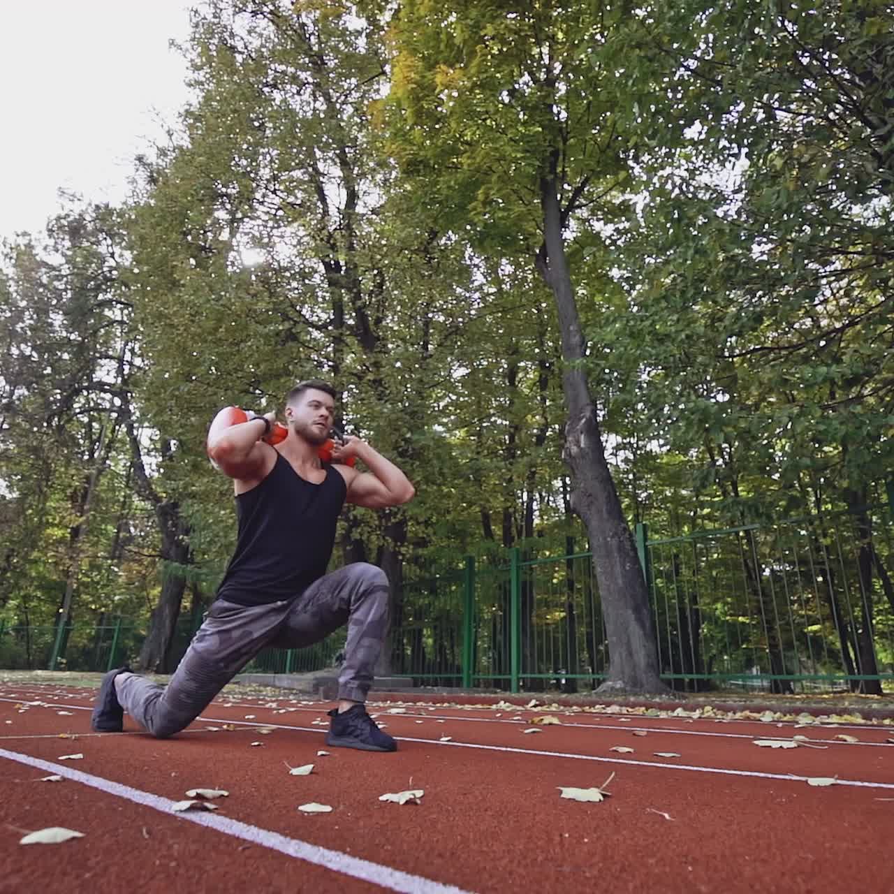 Muscular athlete exercising in the stadium. Young sportsman doing squats with weight while walking. Slow motion.